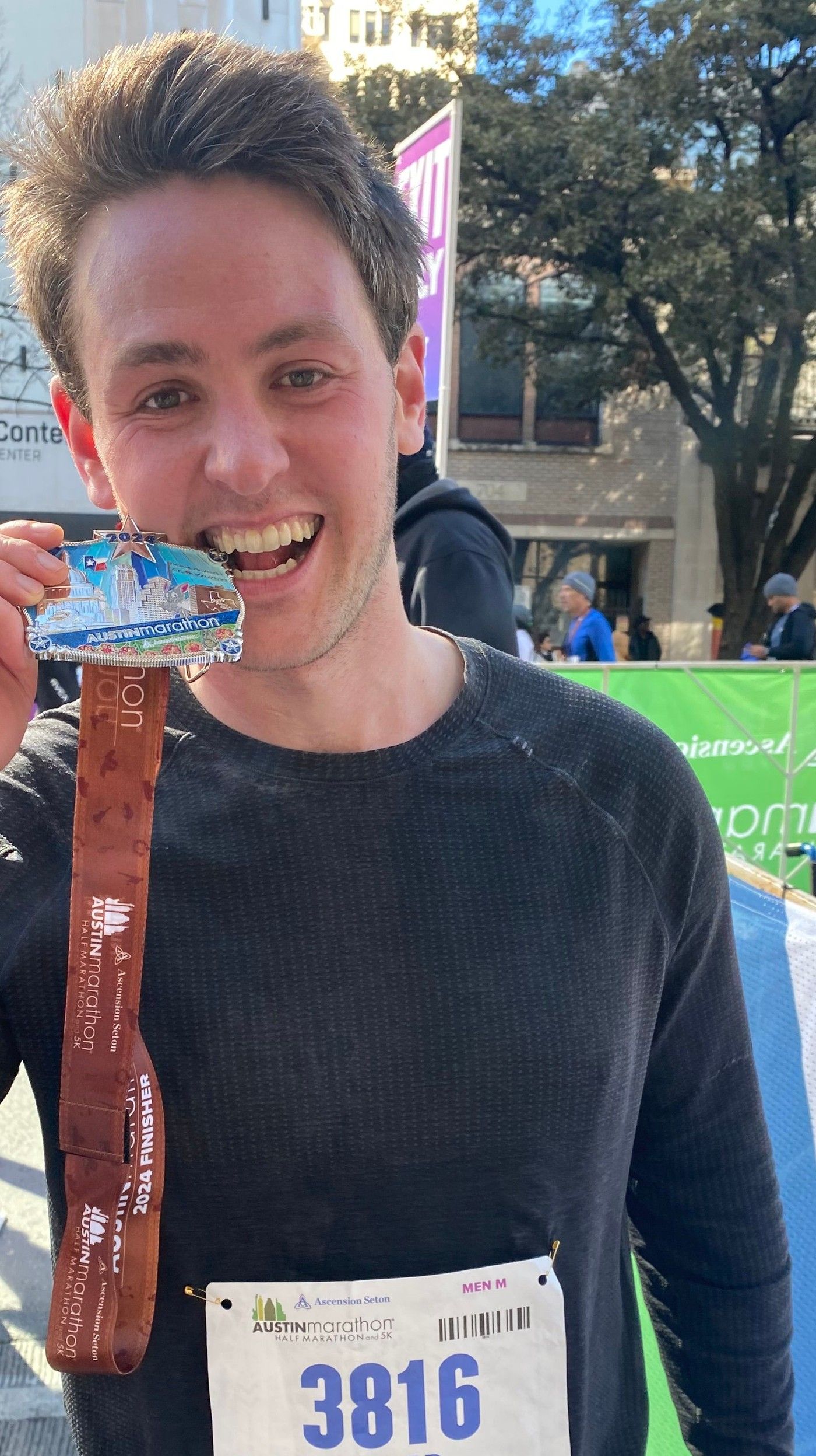 Richard Joseph Spinelli grinning with his 2024 Austin Marathon medal in one hand and a water bottle in the other