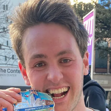 Richard Joseph Spinelli at the 2024 Austin Marathon finish, holding his medal up beside his face